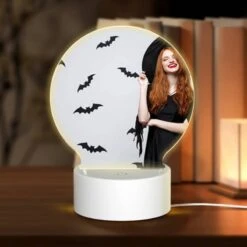 Round Acrylic Night Light, A Woman Wearing A Black Hat And A Black Dress With Bats On The Wall Behind Her.